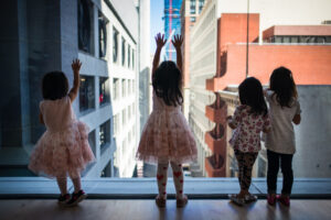 Four little girls looking out towards Natoma street from inside the museum