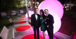 A formally-dressed group poses in front of a giant round purple light fixture